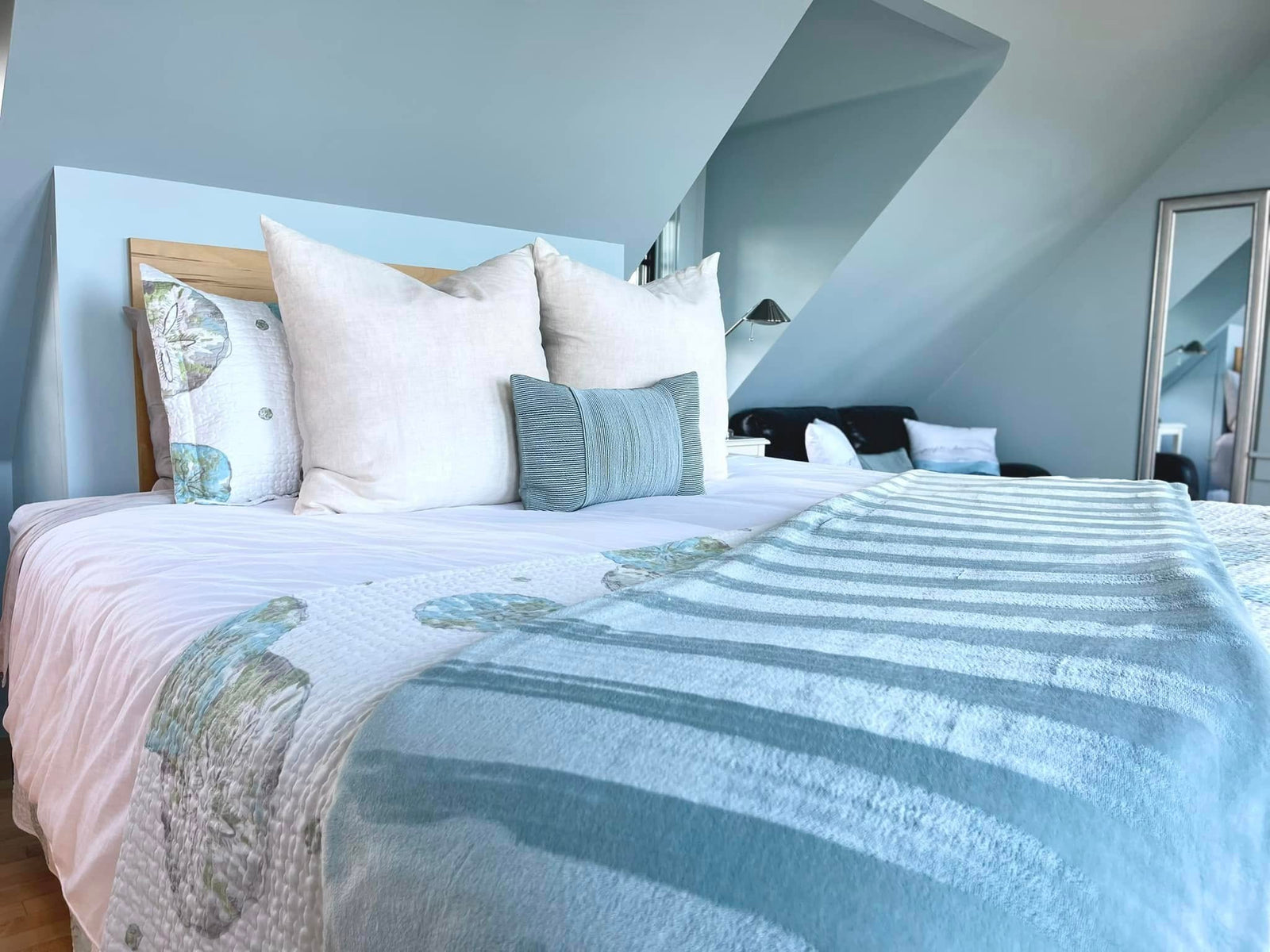 Crisply made bed with white pillows and a blue striped throw