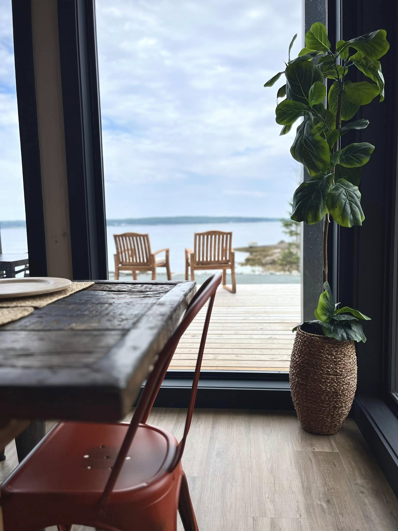 View from a dining table through tall windows to deck chairs and the ocean